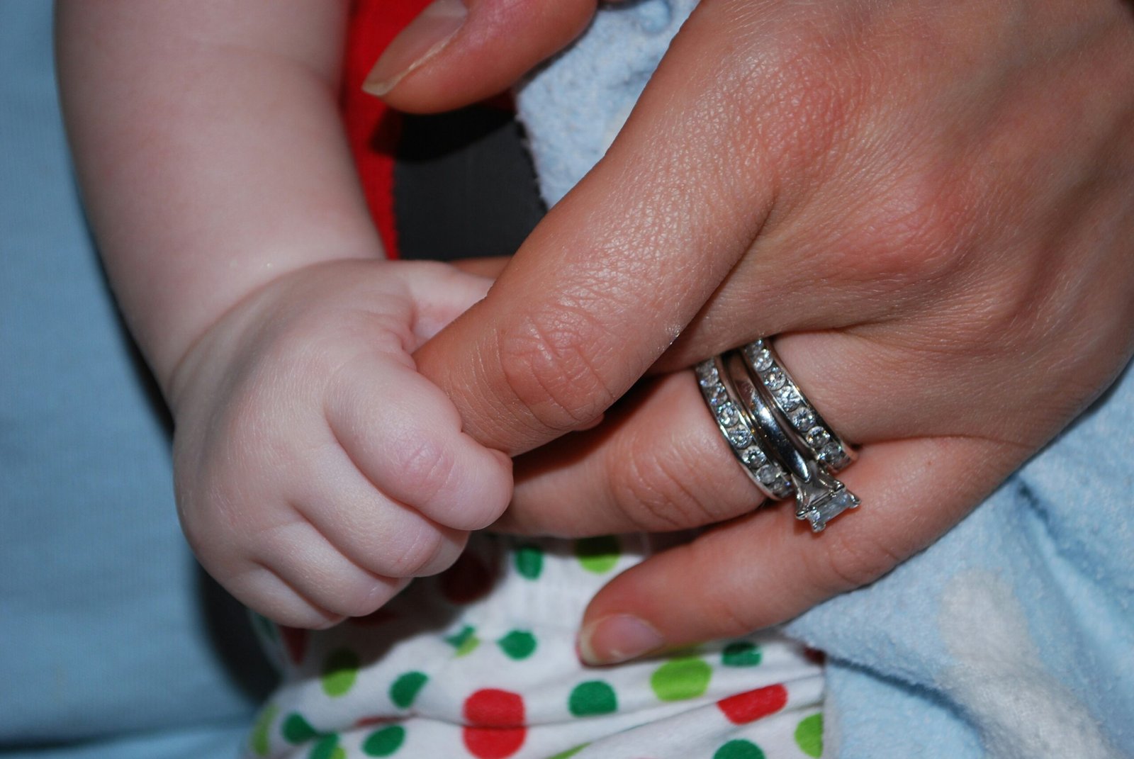 Adult hand holds baby's hand with rings.