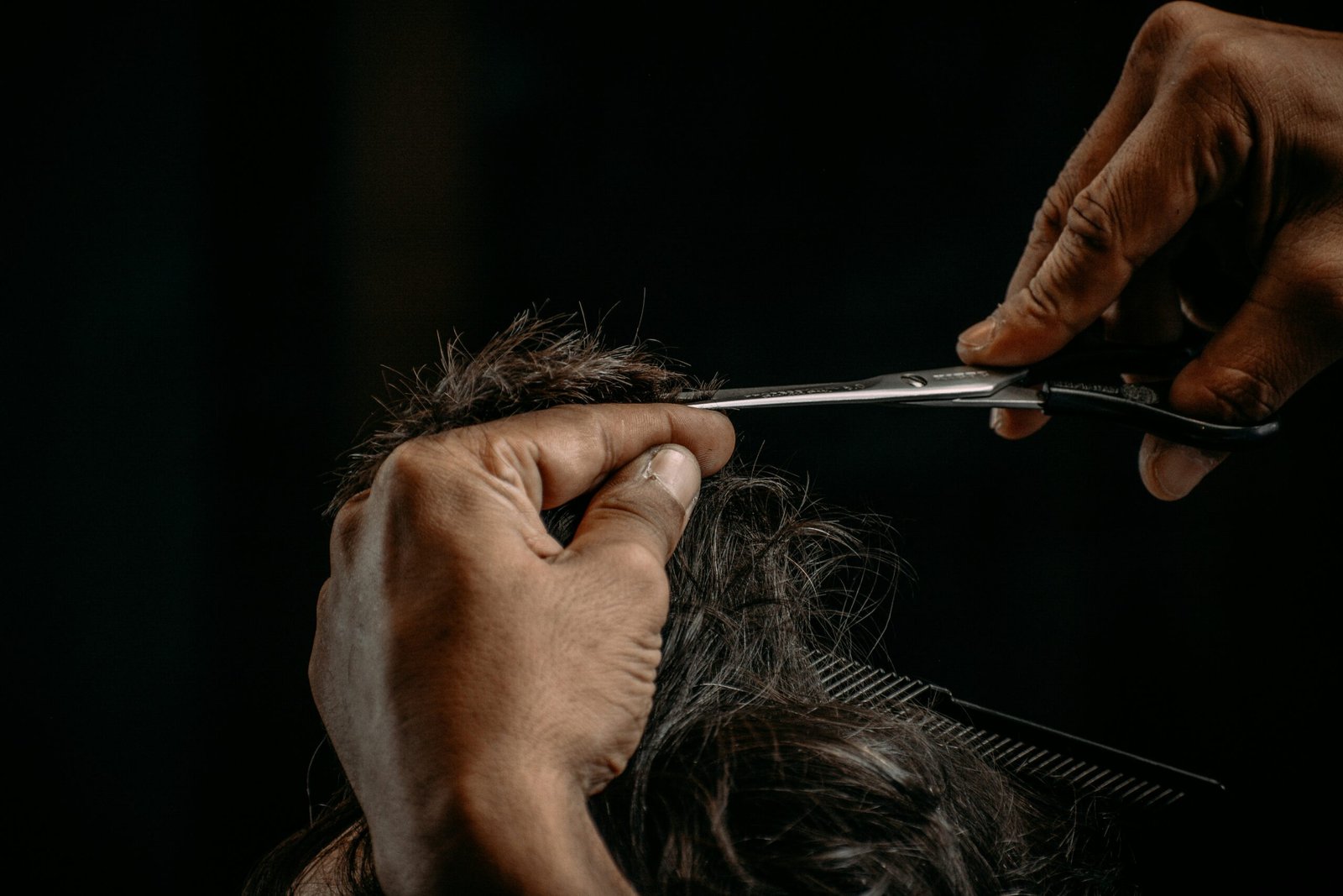 a person cutting a woman's hair with scissors
