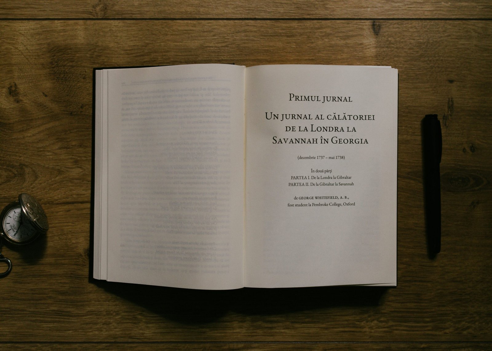 An open book, pen, and pocket watch on wood.