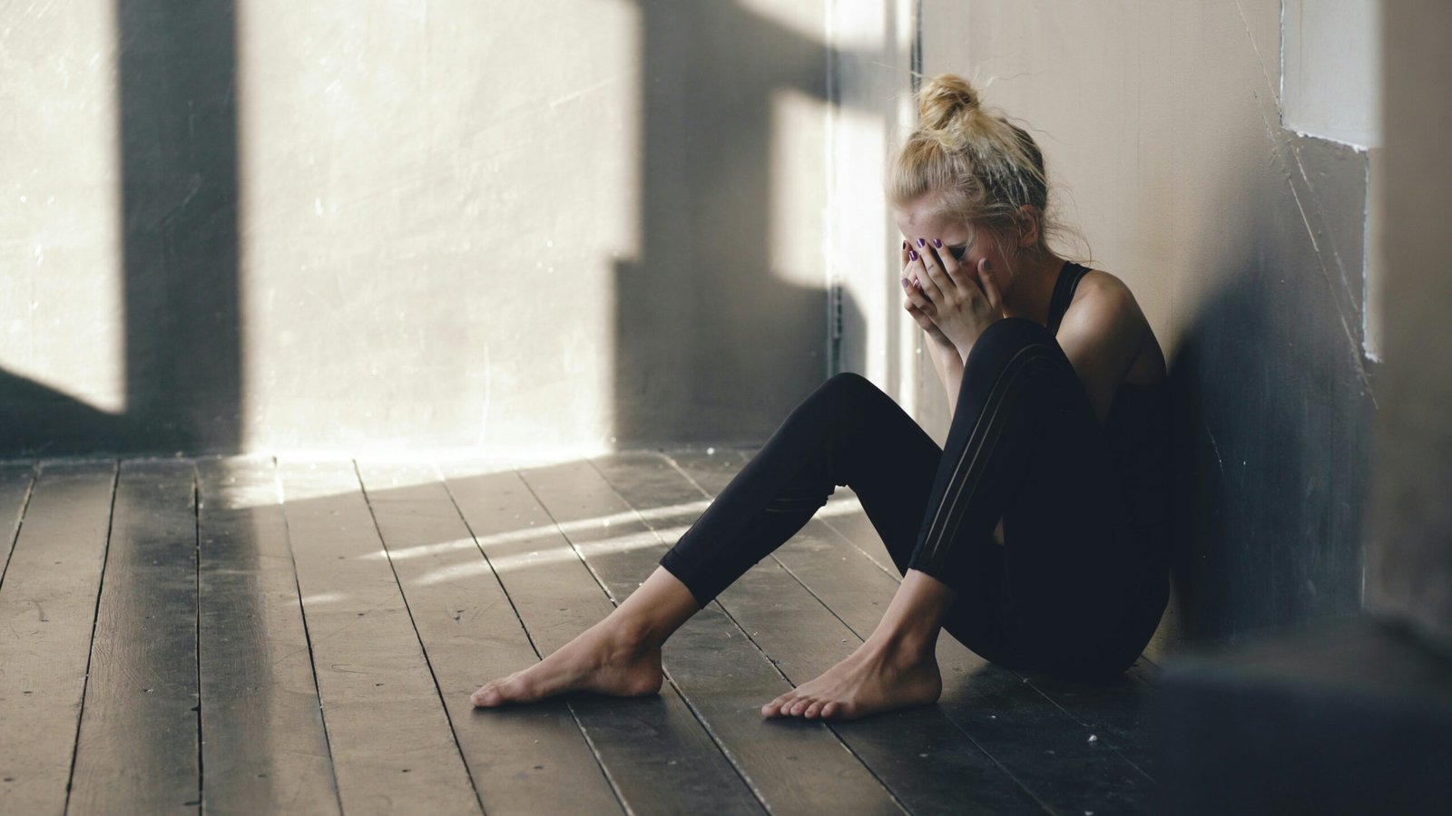Woman sitting on floor, covering face with hands.