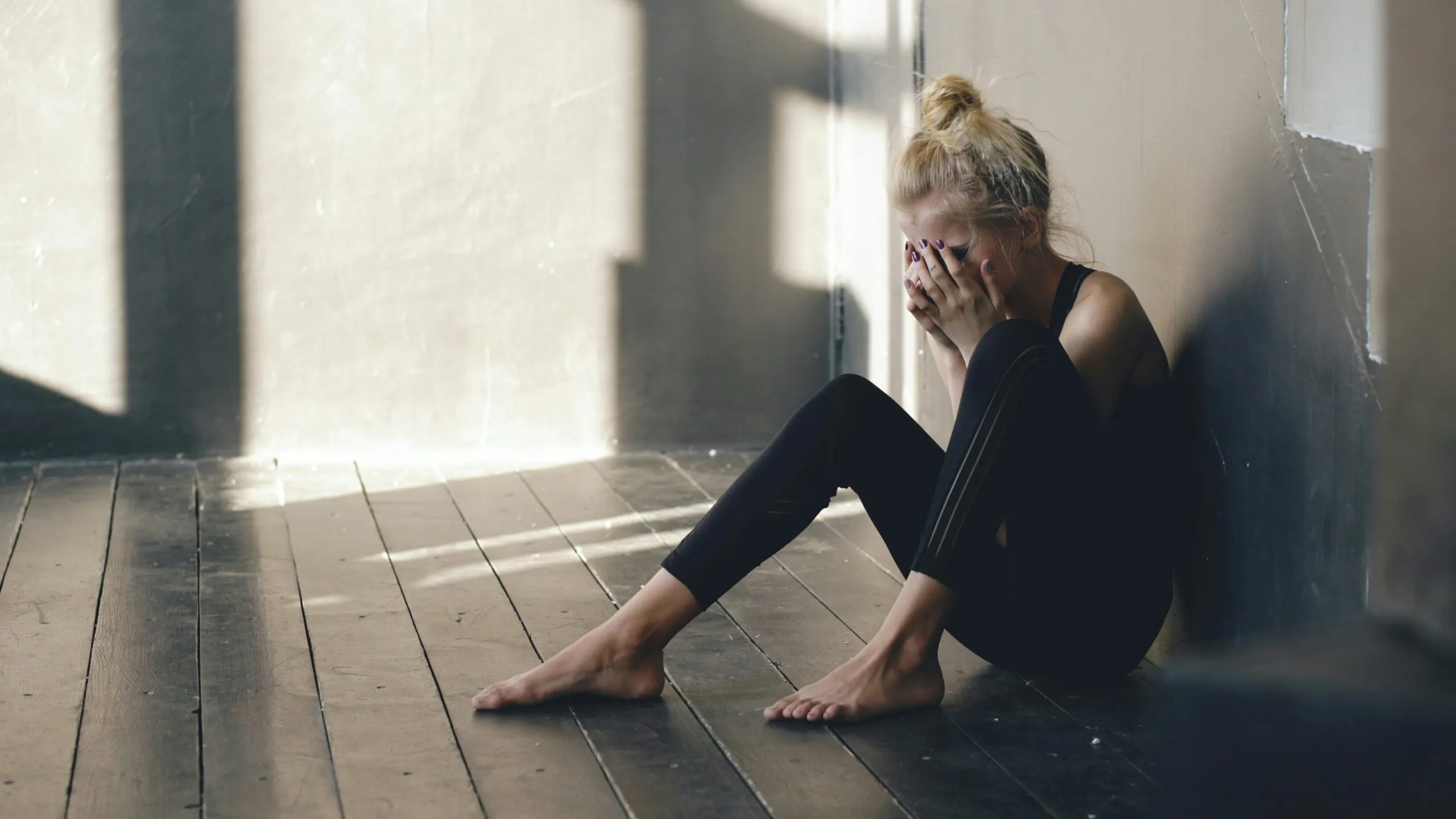 Woman sitting on floor, covering face with hands.