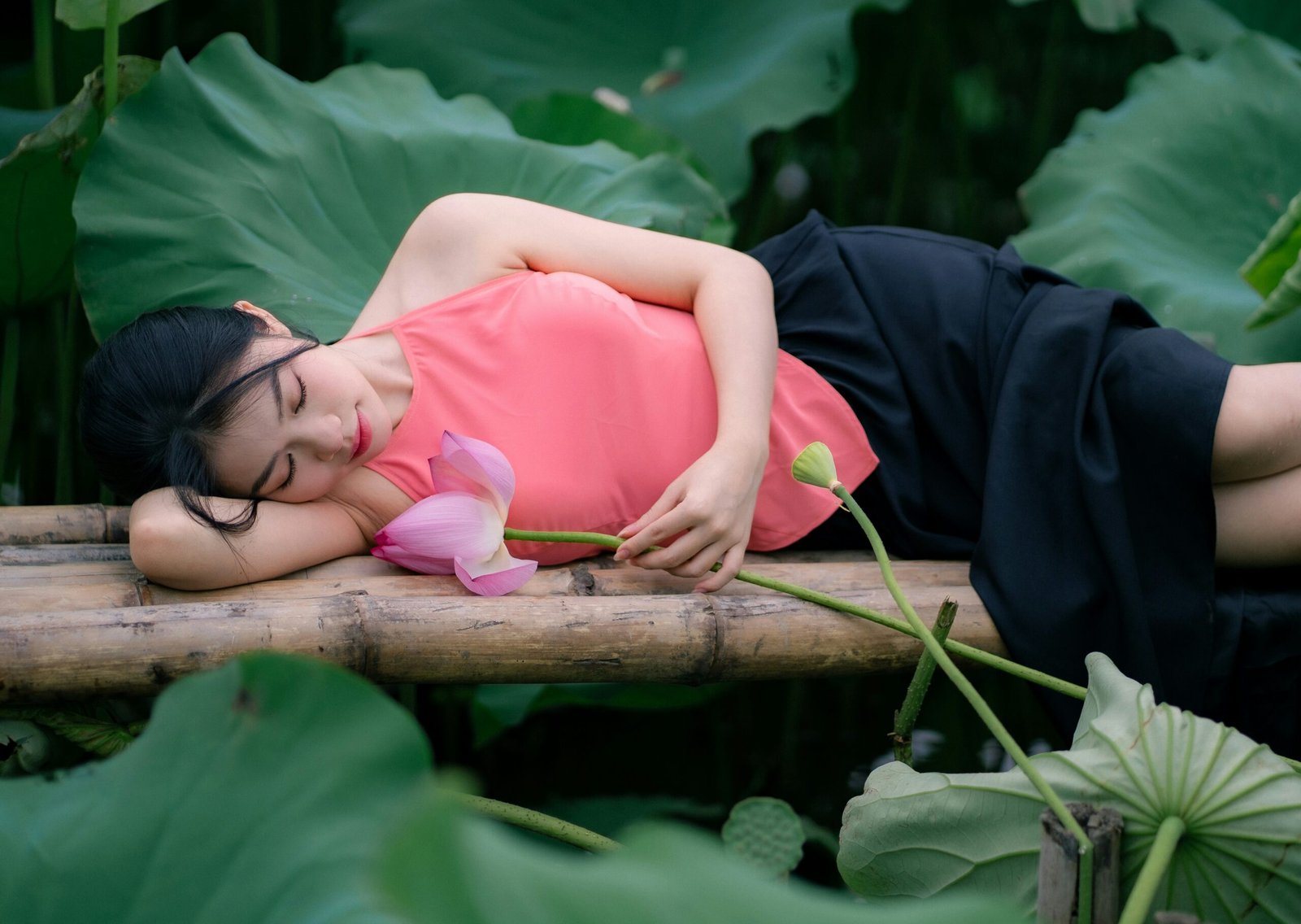 A woman sleeps among lotus leaves and flowers.