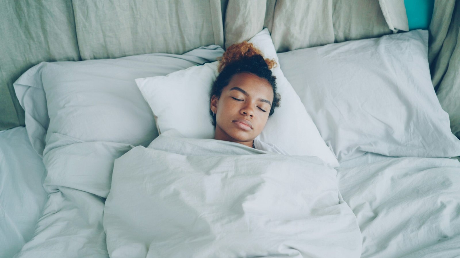 A young woman sleeping peacefully in a white bed.