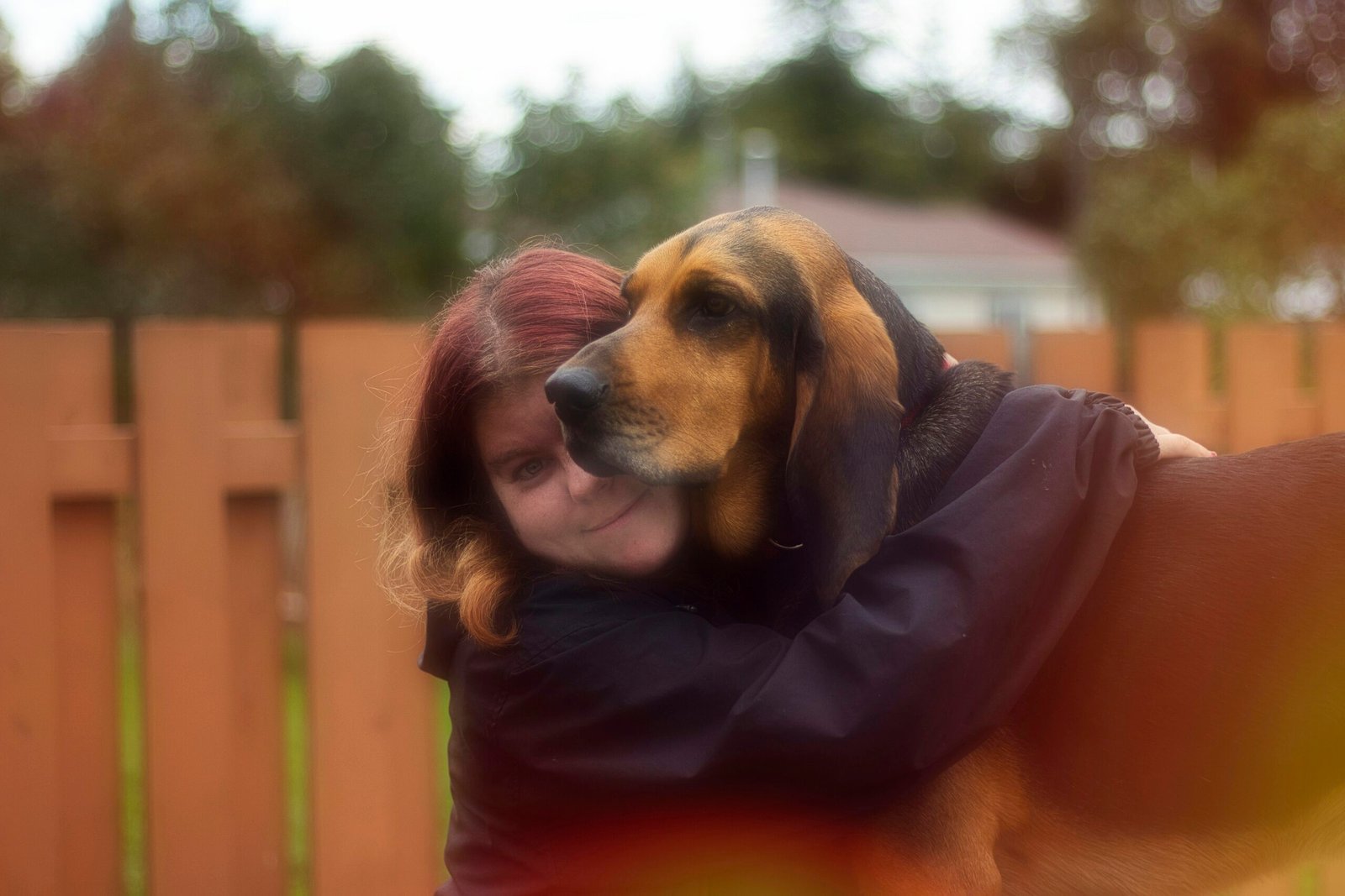 a woman hugging a dog in a fenced in area