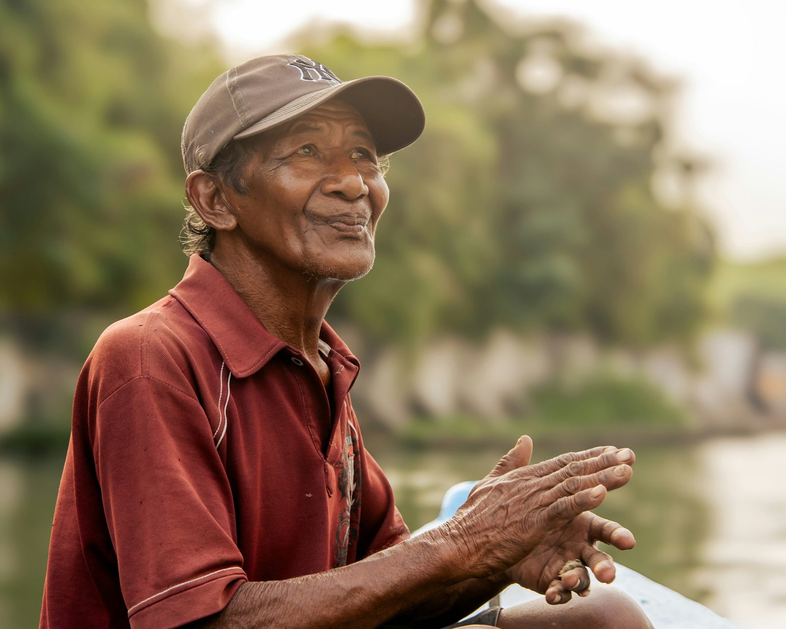 Elderly man in a cap and shirt clasps hands