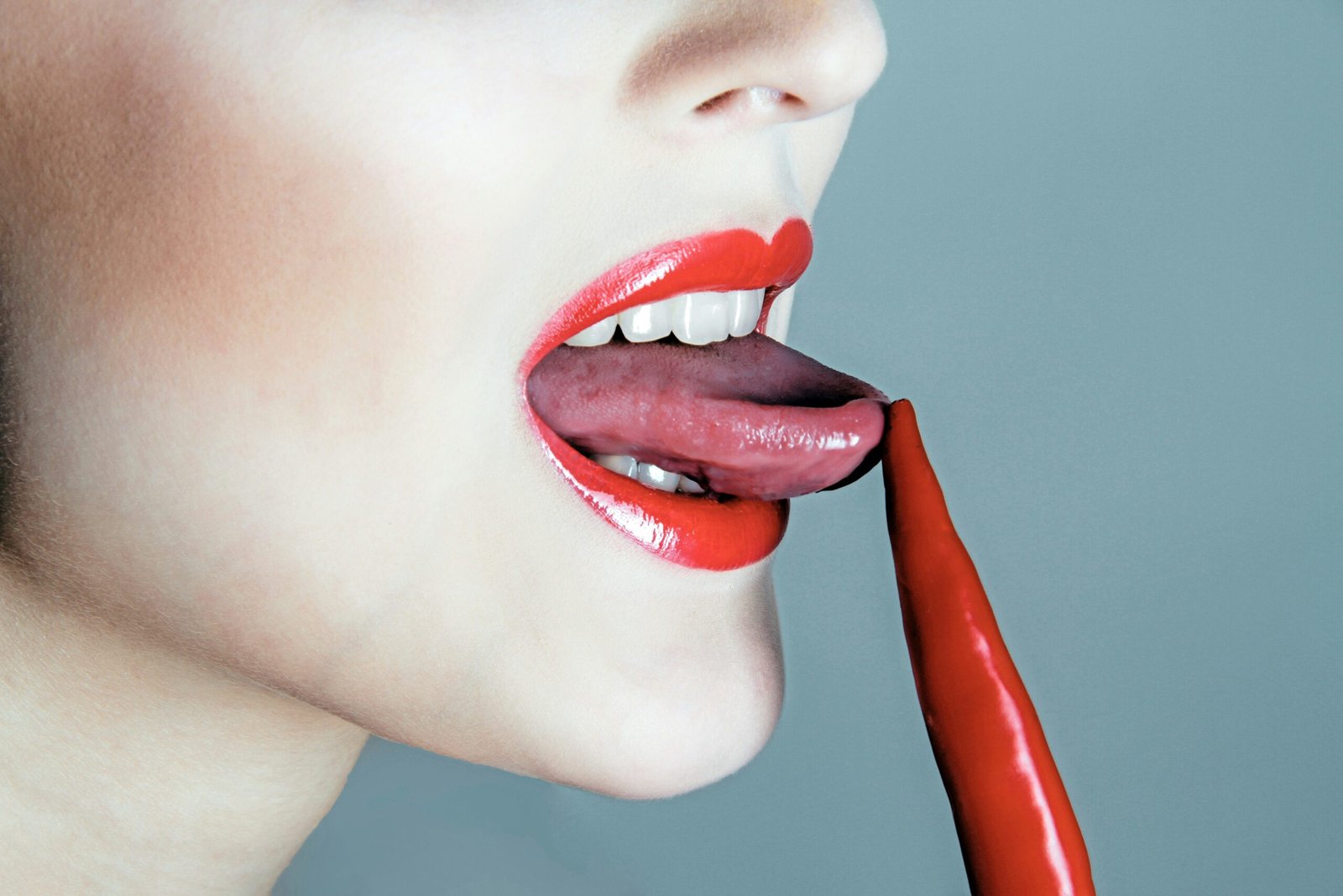 Woman licking a red chili pepper.