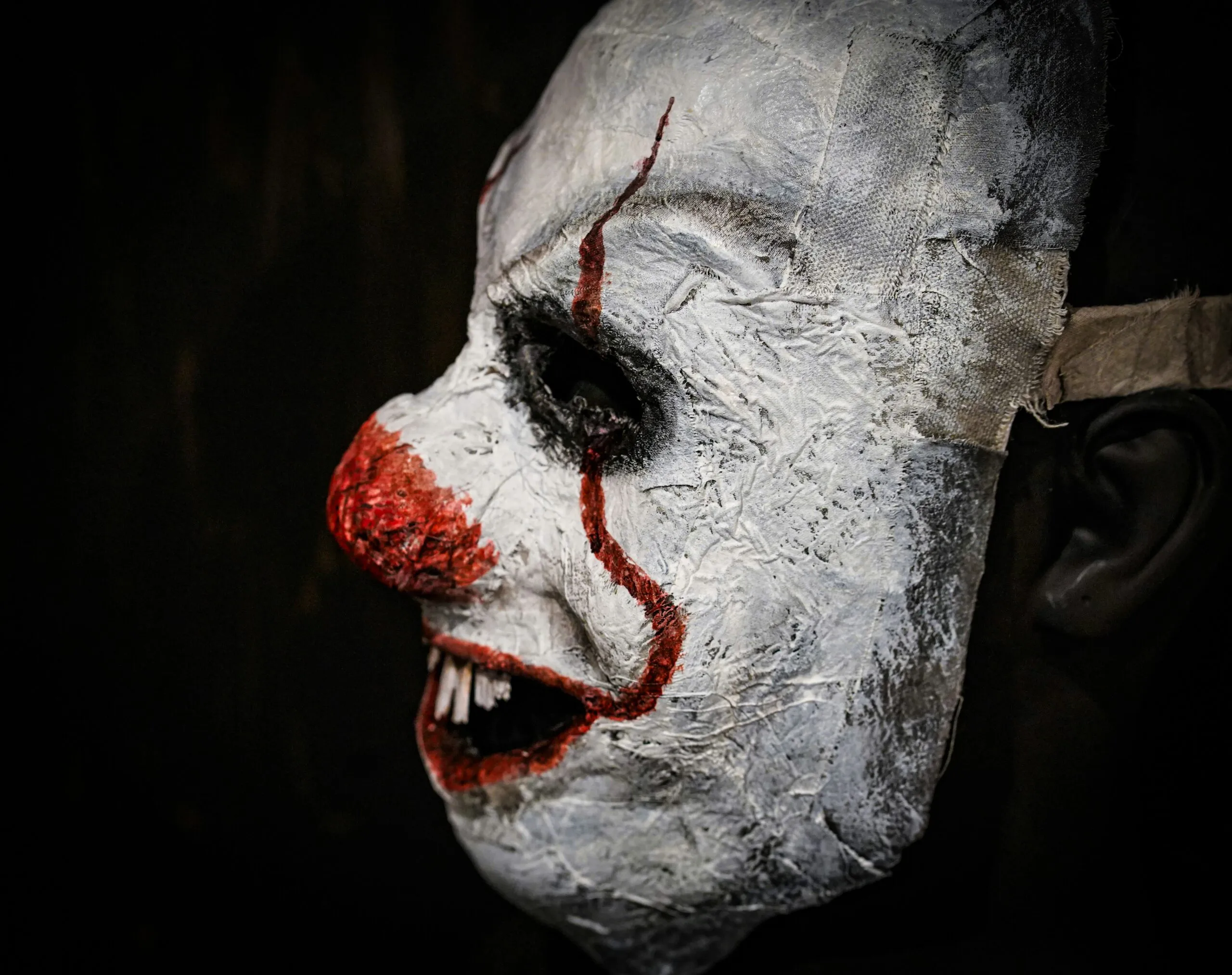 A creepy clown mask with white face and red nose.