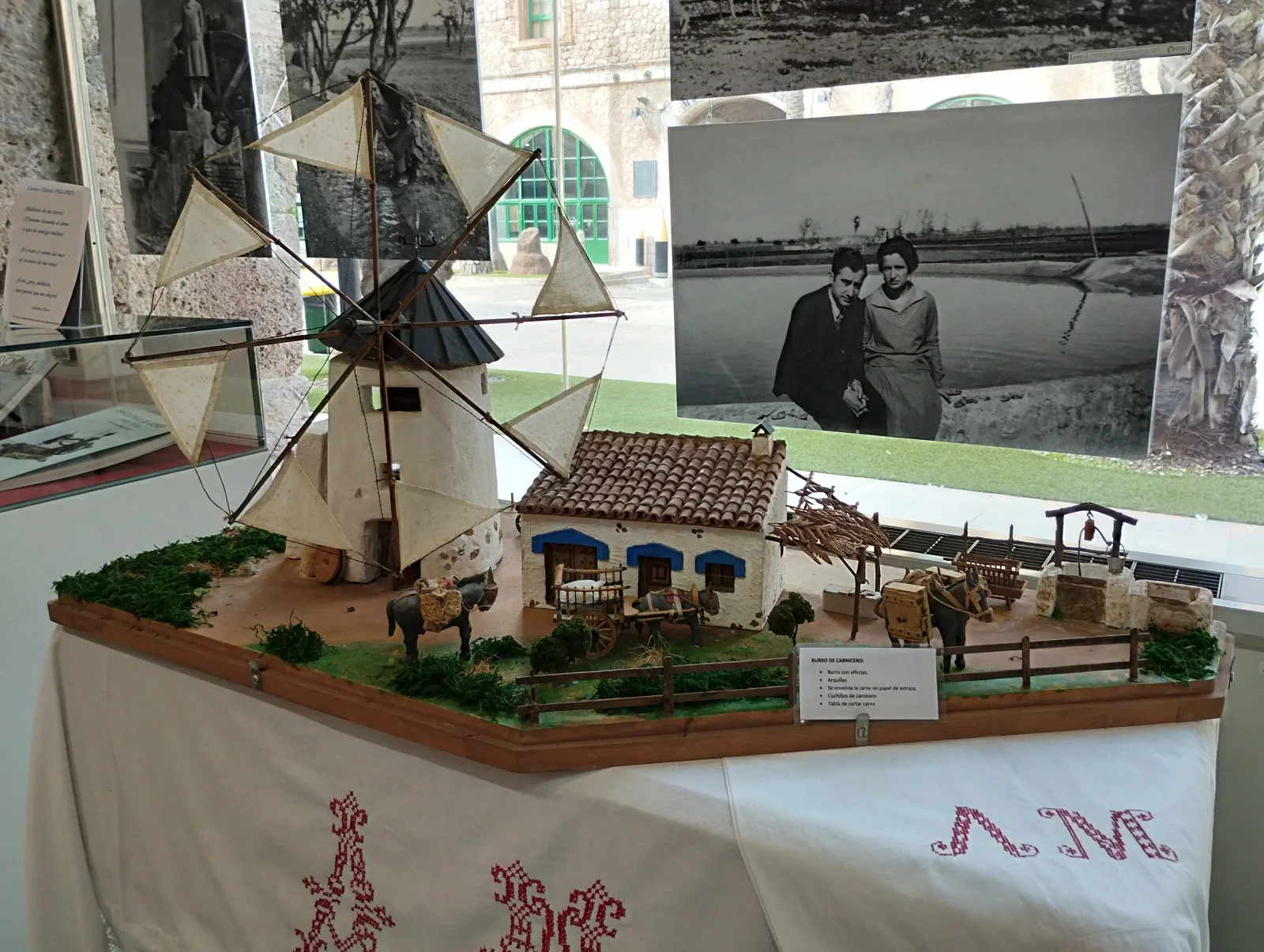 Model of a windmill in the Campo de Cartagena, created by the miniaturist Antonio Madrid López and displayed in the Municipal Archive of Cartagena (Spain) during the temporary exhibition "The Campo de Cartagena in miniature by Antonio Madrid López: a stage for making visible the role of women in rural areas". It also shows examples of rustic use of donkeys, and a house built according to the patterns of vernacular architecture.
Hanging behind the model is a photograph of the poets Antonio Oliver and Carmen Conde in the countryside.