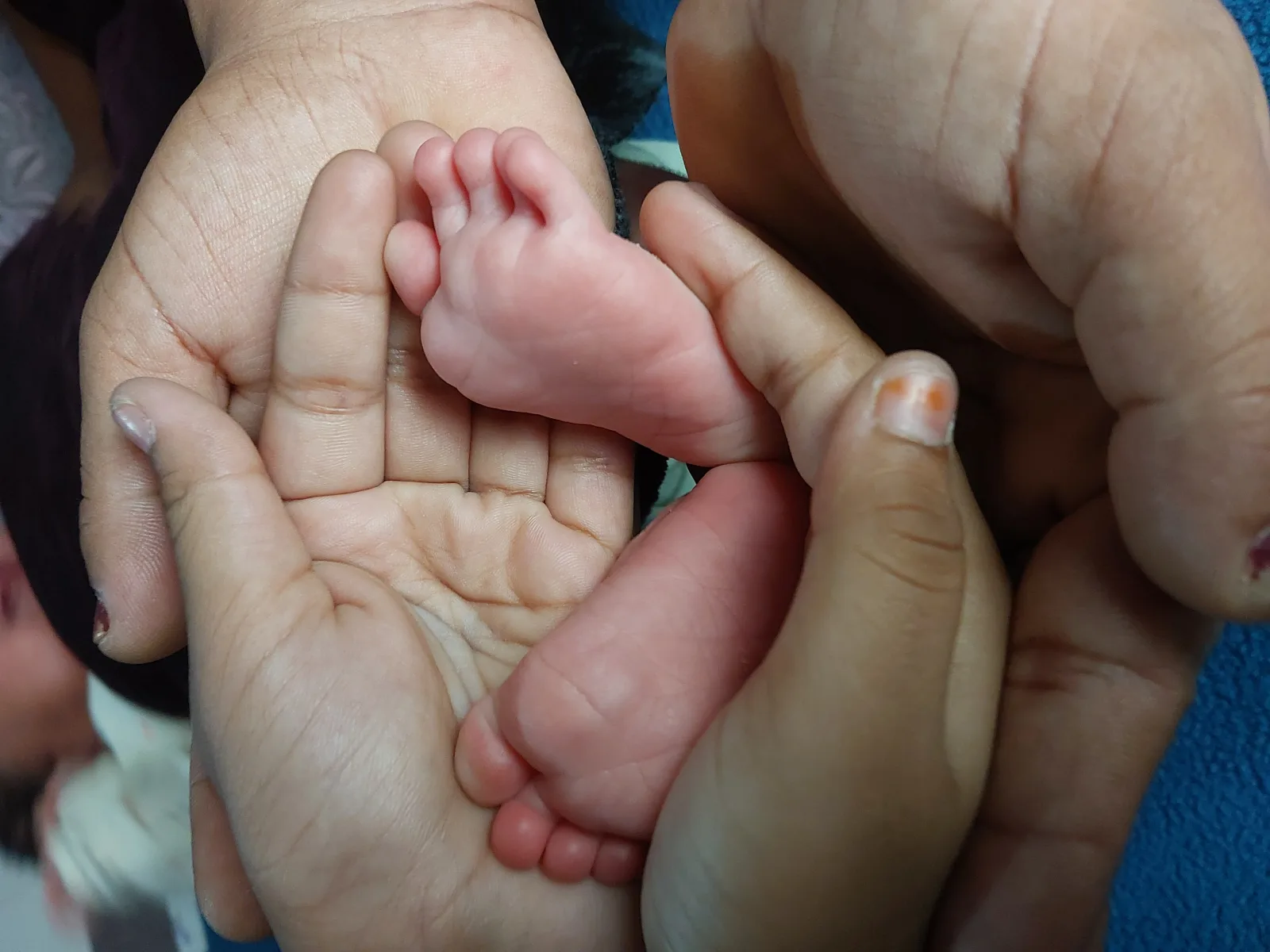 Close-up of a newborn baby’s feet gently held by family members’ hands, symbolizing care, bonding, and the welcoming of a new life within an Indian family setting.