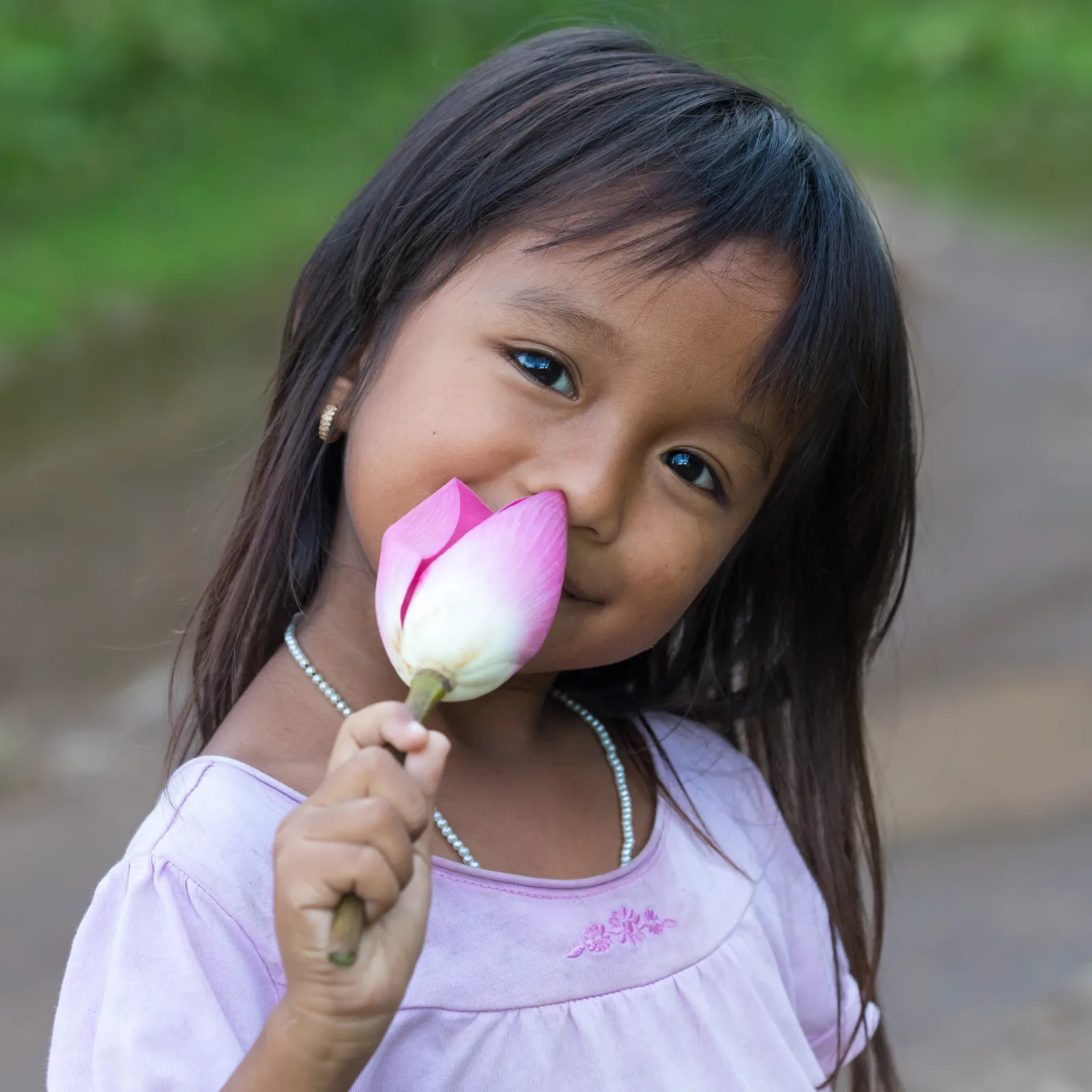 Smiling little girl looking at the viewer, the head tilted to the left and holding a bud of Nelumbo nucifera (lotus flower) in her right hand, in Don Det, Laos
