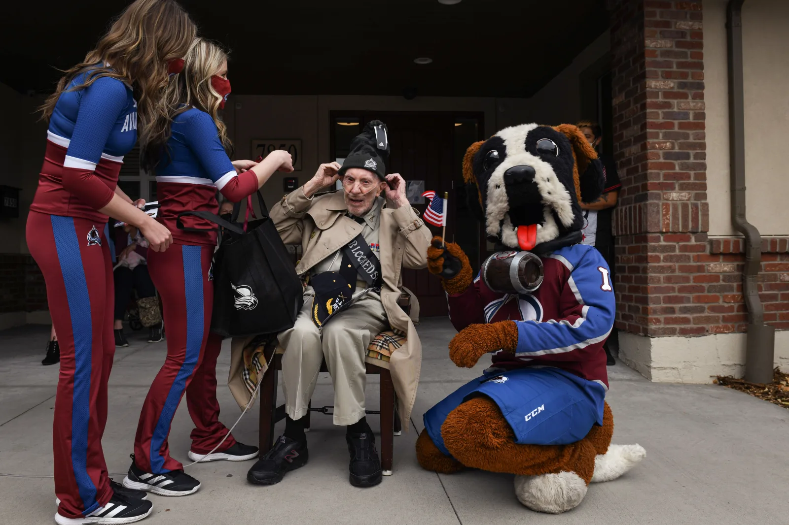 Retired U.S. Army Maj. David Howie puts on a hat given to him by cheerleaders from the Colorado Avalanche during his surprise 100th birthday parade in Wheat Ridge Colo., Nov. 8, 2021. Members from Buckley Space Force Base and Fort Carson honored Howie's service by hosting a surprise birthday party outside of his assisted living home, which included a motorcycle procession, Colorado Avalanche cheerleaders, a police car drive-by and much more. (U.S. Space Force photo by Senior Airman Danielle McBride)