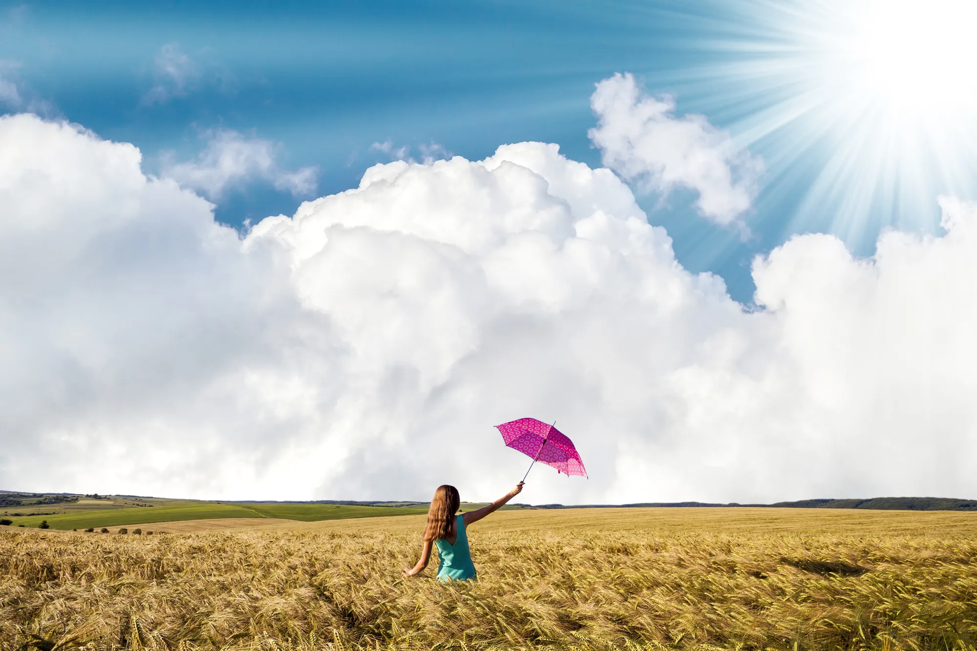 Beauty young girl outdoors enjoying nature. Beautiful teenage model girl in blue dress with red umbrella on the wheat field in rays of sun light.