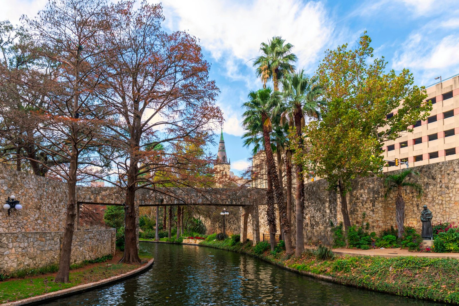 a river running through a lush green park next to a tall building