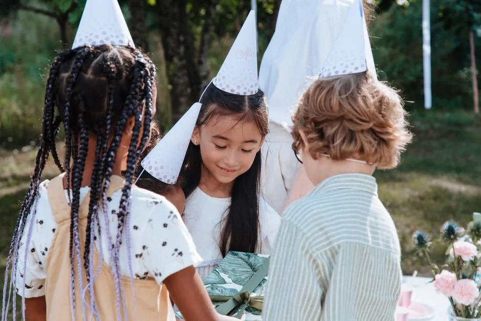 Children celebrating a birthday party outdoors with friends and gifts in a garden setting.