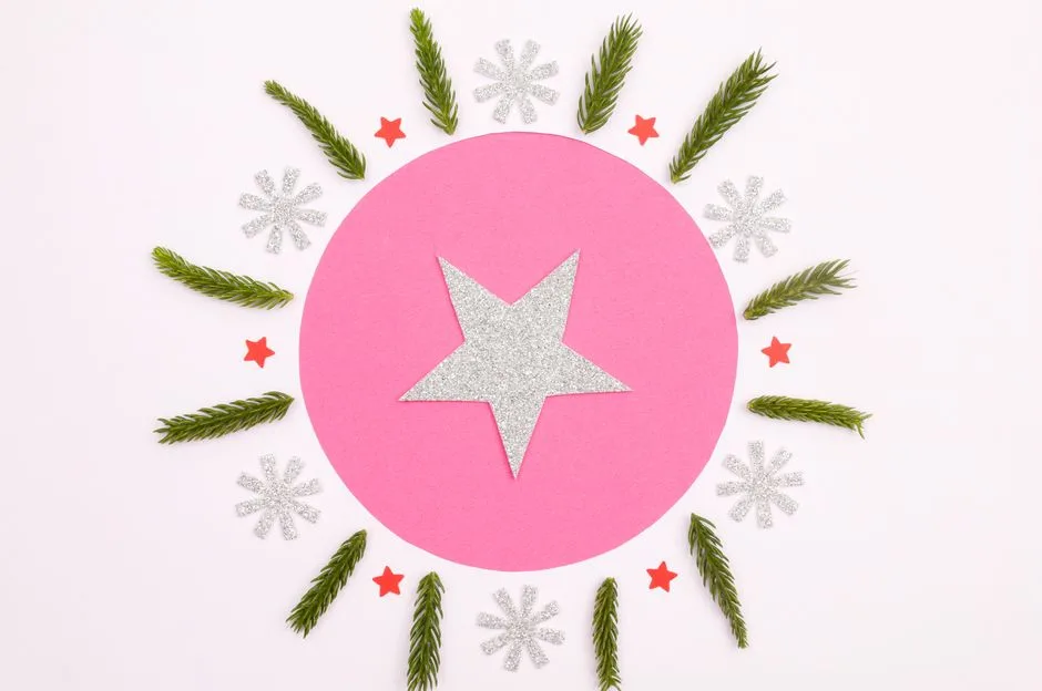 Creative Christmas card design with glitter star and pine leaves on pink background.
