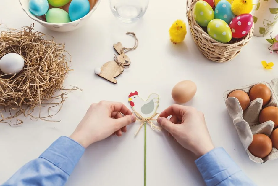 Hands arranging Easter decorations on a table with colorful eggs and festive decor.