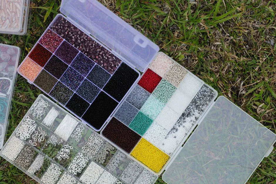 Top view of colorful beads organized in plastic boxes on grassy ground, ideal for crafting and hobbyists.