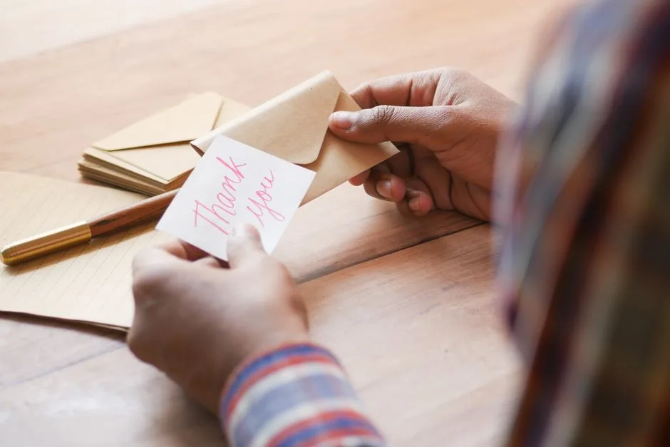 Close-up of hands holding a thank you note in an envelope on a table.