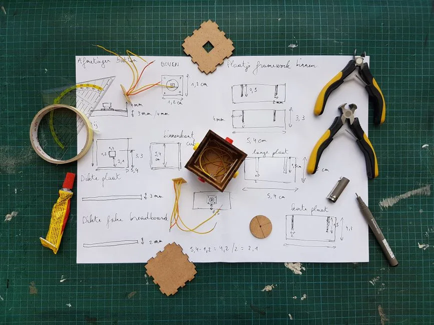 Overhead view of DIY electronics project with components and tools on grid mat.