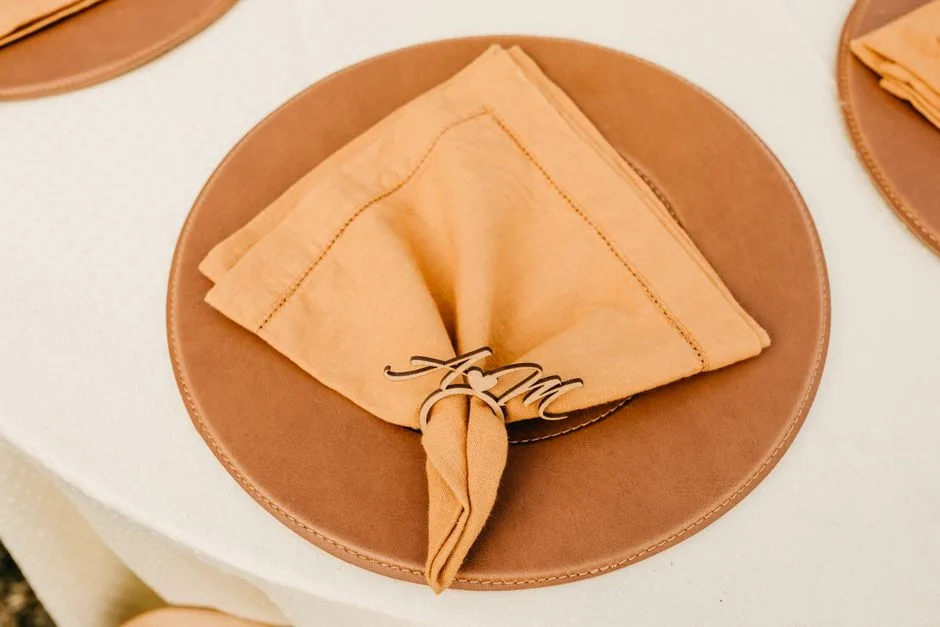 Close-up of a sophisticated table setting featuring a folded napkin with a decorative ring on a brown plate.