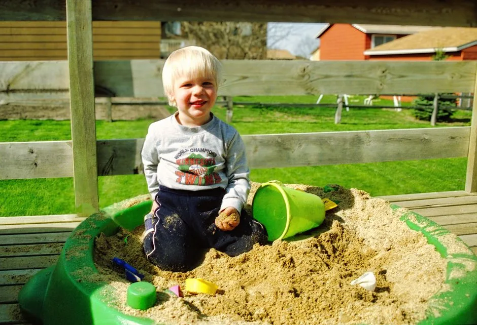 A cheerful toddler enjoying playtime in a backyard sandbox on a sunny day.