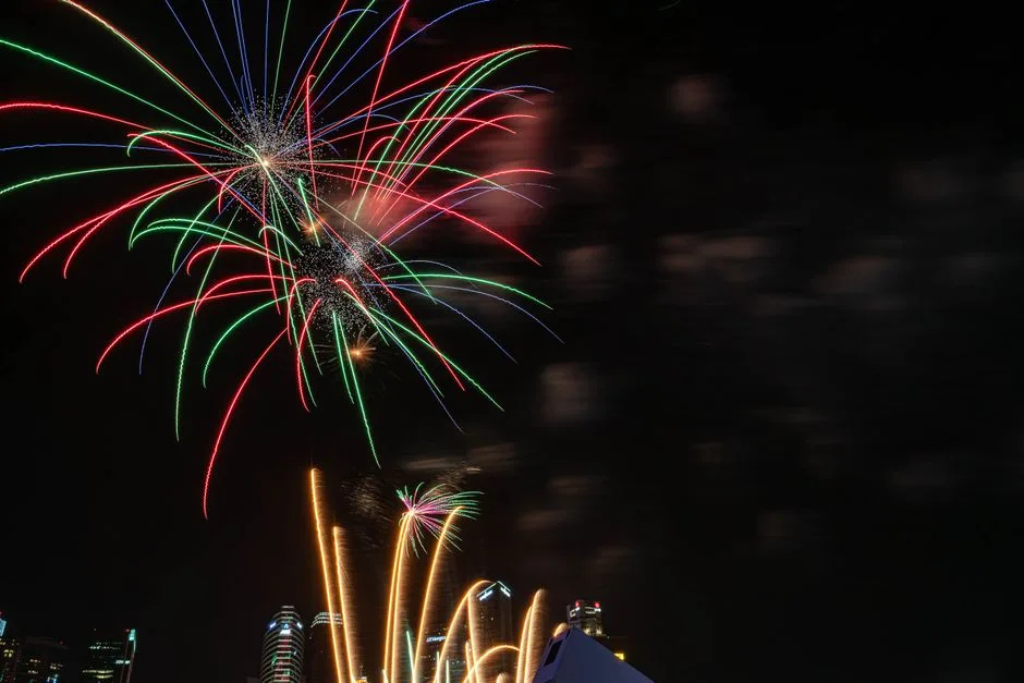 Vibrant fireworks light the night sky over a city skyline, capturing a festive atmosphere.
