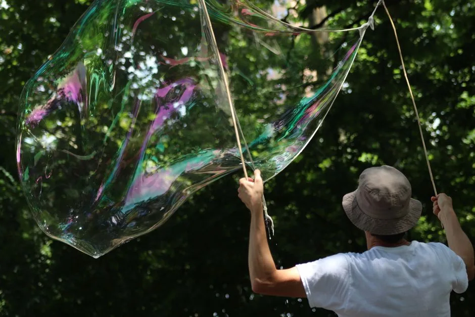 A person making a giant iridescent bubble outside, showcasing a playful summer activity.