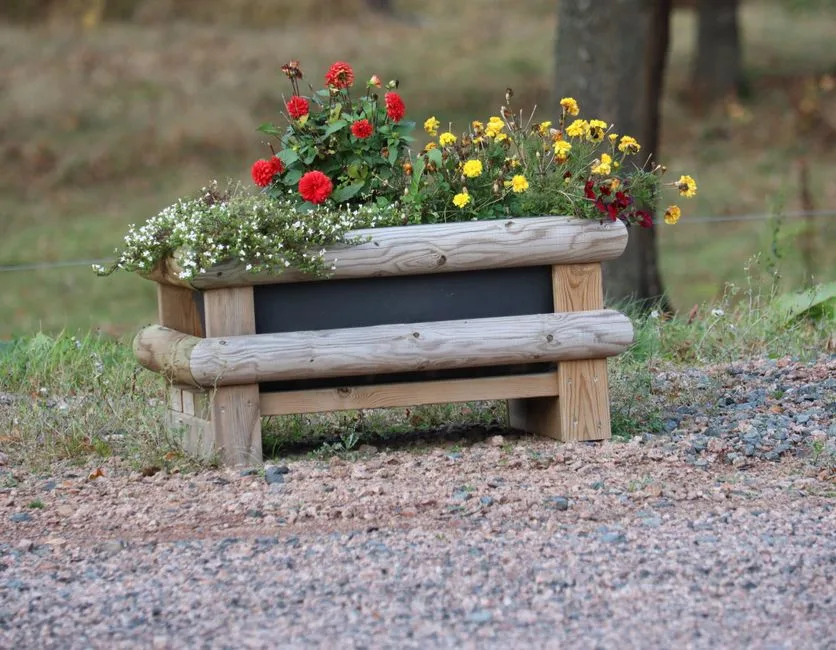 Rustic wooden planter with vibrant red and yellow blooms in an outdoor garden setting.