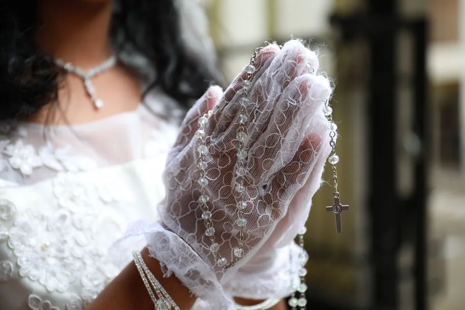 Hands in prayer with lace gloves holding rosary beads, symbolizing a First Communion ceremony.