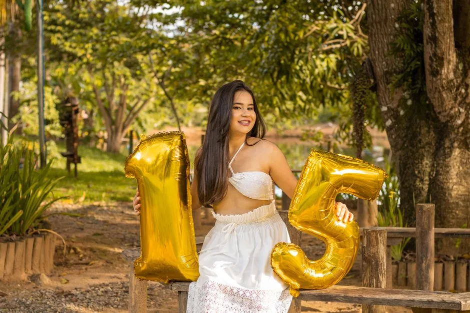 A joyful young woman in white dress celebrating her 15th birthday with balloons outdoors.
