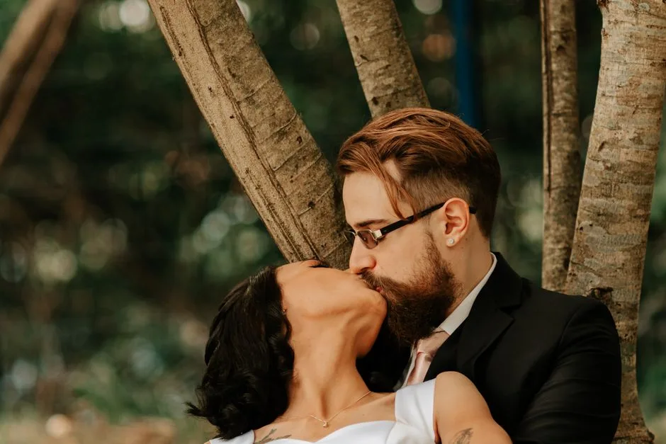 A loving couple shares a romantic kiss under a tree in an outdoor setting.