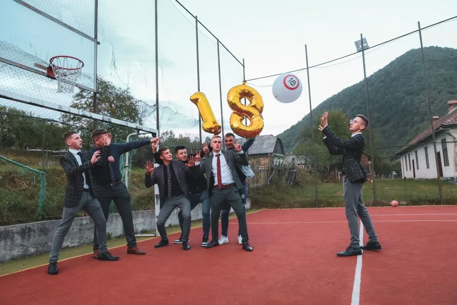 A group of young men celebrating an 18th birthday on an outdoor basketball court with balloons.