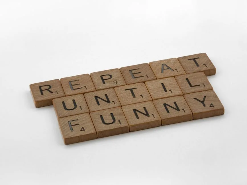 Wooden Scrabble tiles spelling 'repeat until funny' on a white background, conveying humor.