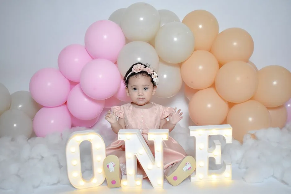Charming baby girl celebrates her first birthday surrounded by colorful balloons.