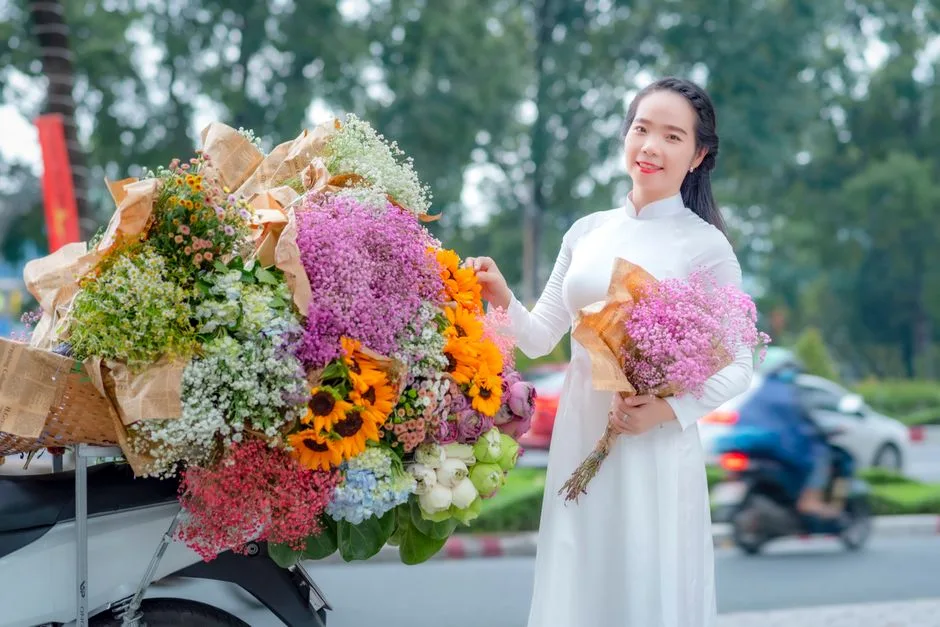 A woman in a white dress happily holding a bouquet of vibrant flowers outdoors.