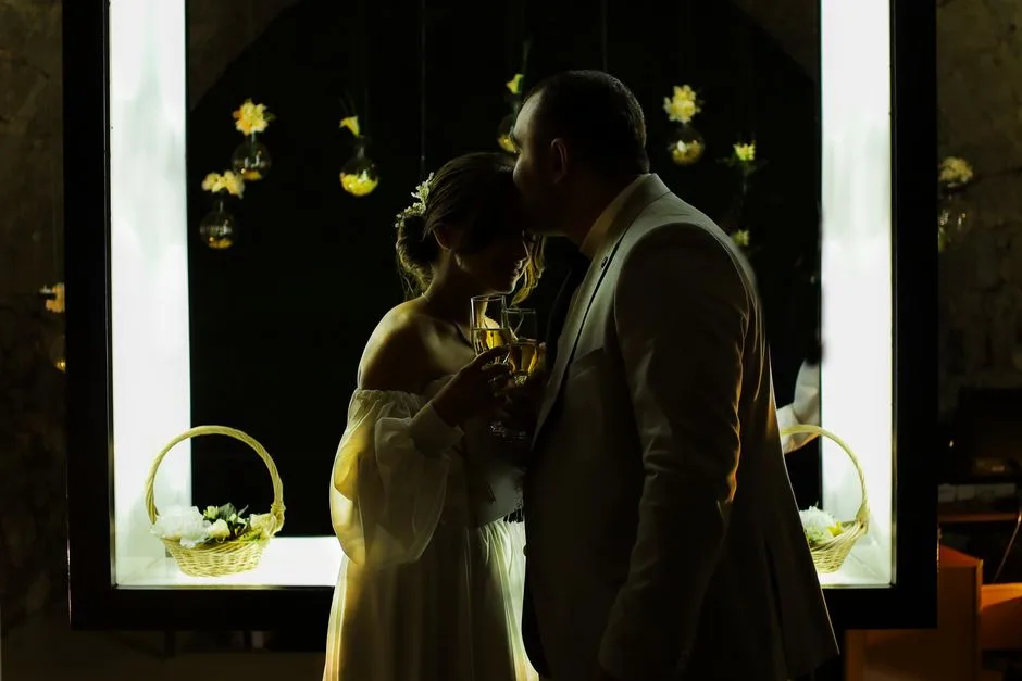 Newlyweds share a romantic moment under soft light, celebrating with champagne.