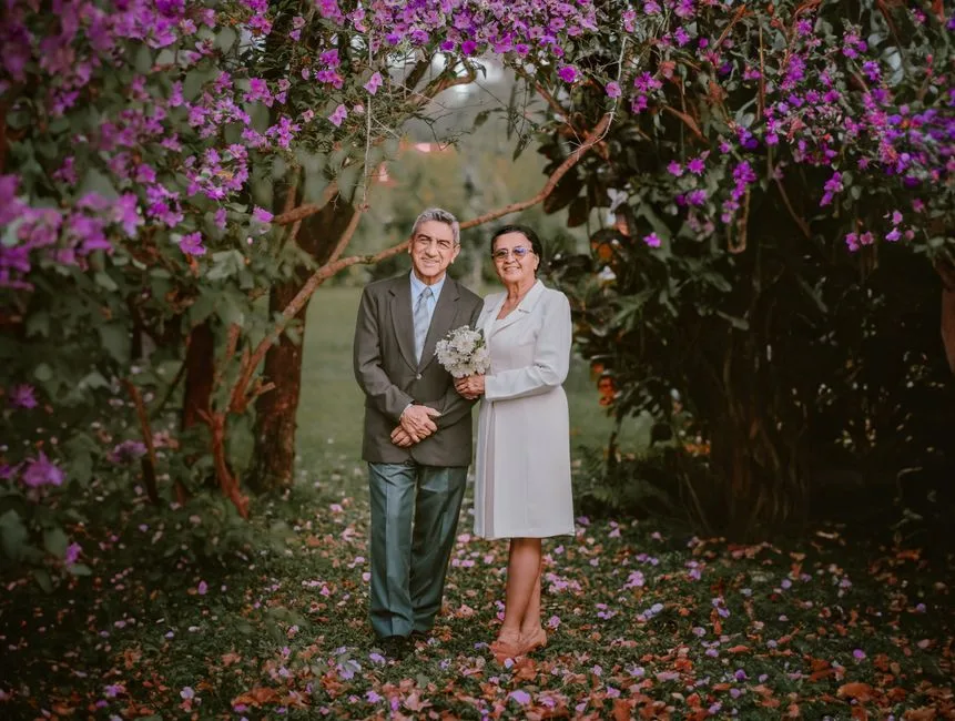 Senior couple standing in a garden under vibrant purple flowers, capturing a moment of love and elegance.