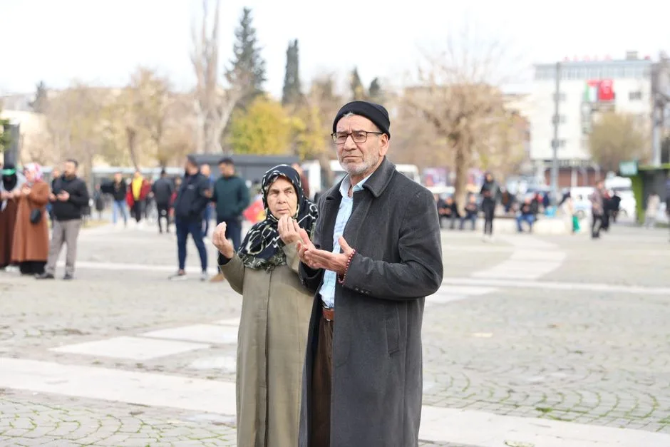 An elderly couple praying together in an open town square setting.
