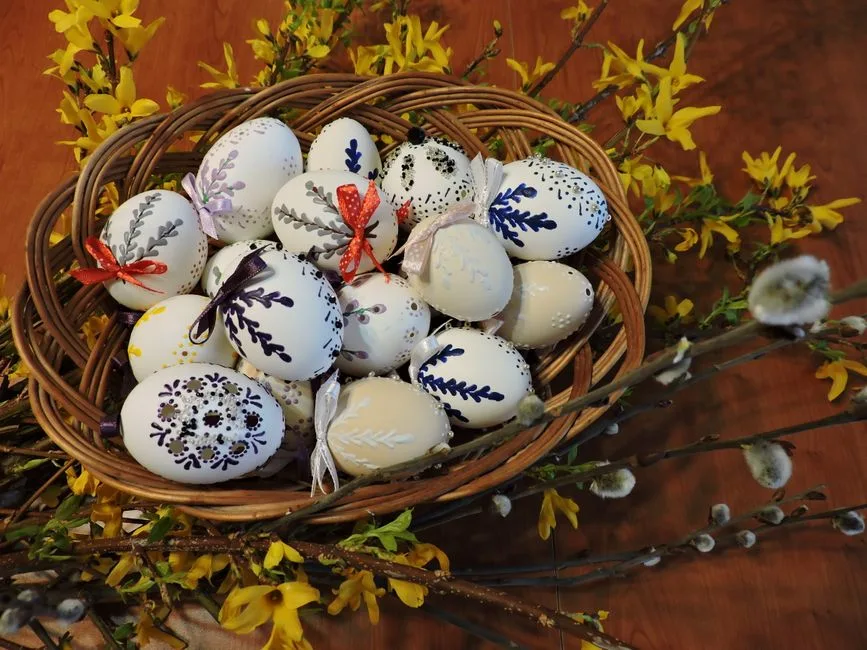 A close-up of a basket filled with beautifully decorated Easter eggs surrounded by yellow spring flowers.