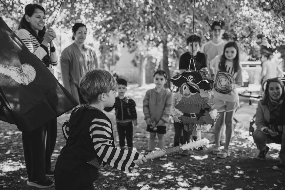 Children at a pirate-themed birthday party outdoors, ready to hit the piñata.