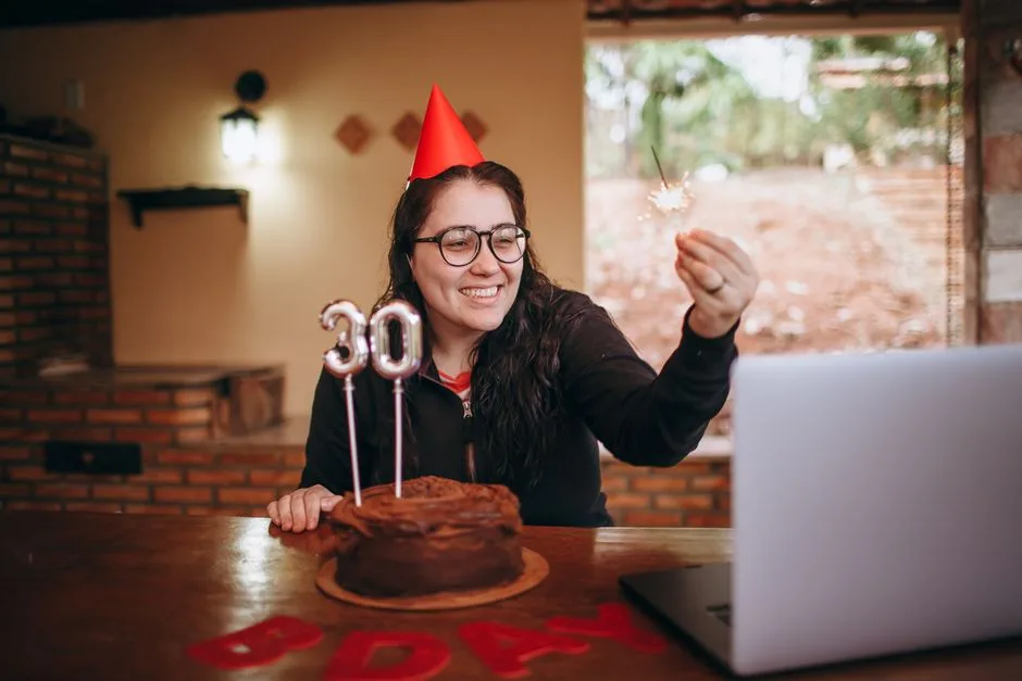 A woman enjoys her 30th birthday with a cake and sparkler, celebrating via video call.