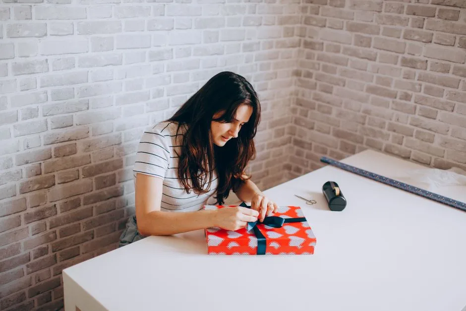 Woman gift wrapping at table in cozy room with brick walls, showcasing creativity and leisure.