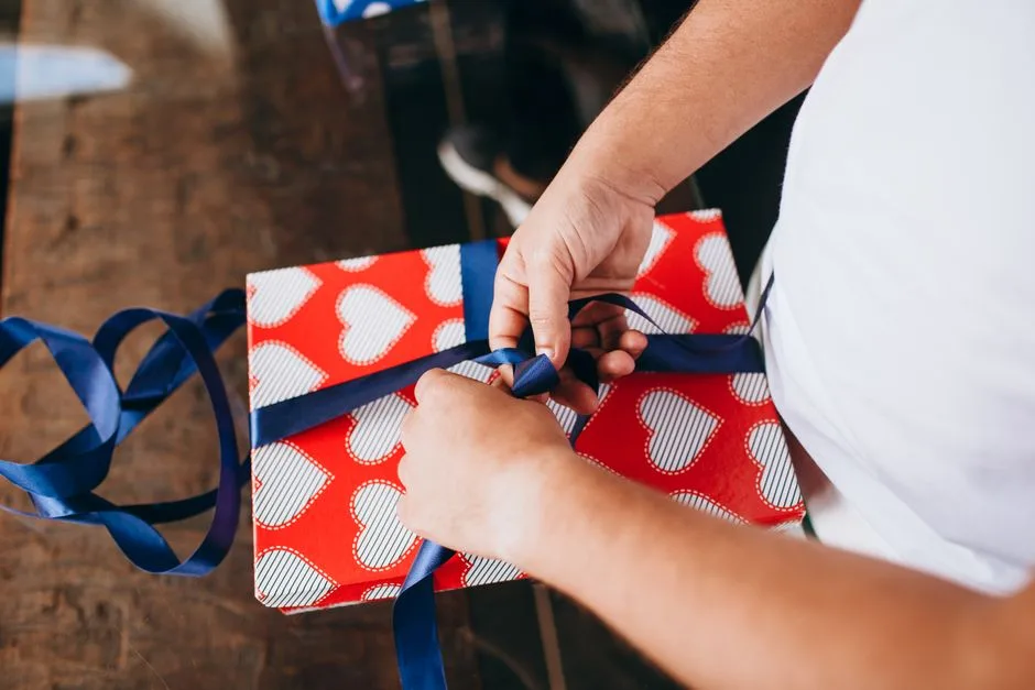 Hands tying a blue ribbon on a heart-patterned gift, symbolizing love and celebration.