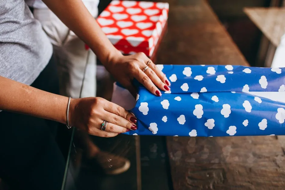 Close-up of a woman wrapping a gift with blue cloud-patterned paper indoors.