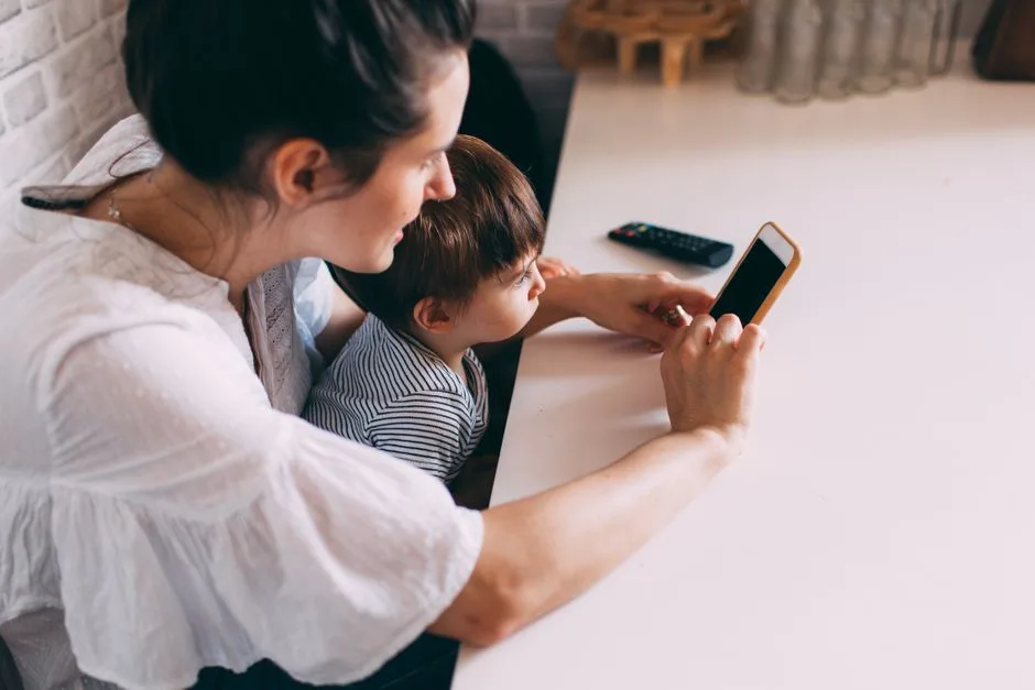 A mother and her child engaging with a smartphone indoors. Perfect for family and technology themes.