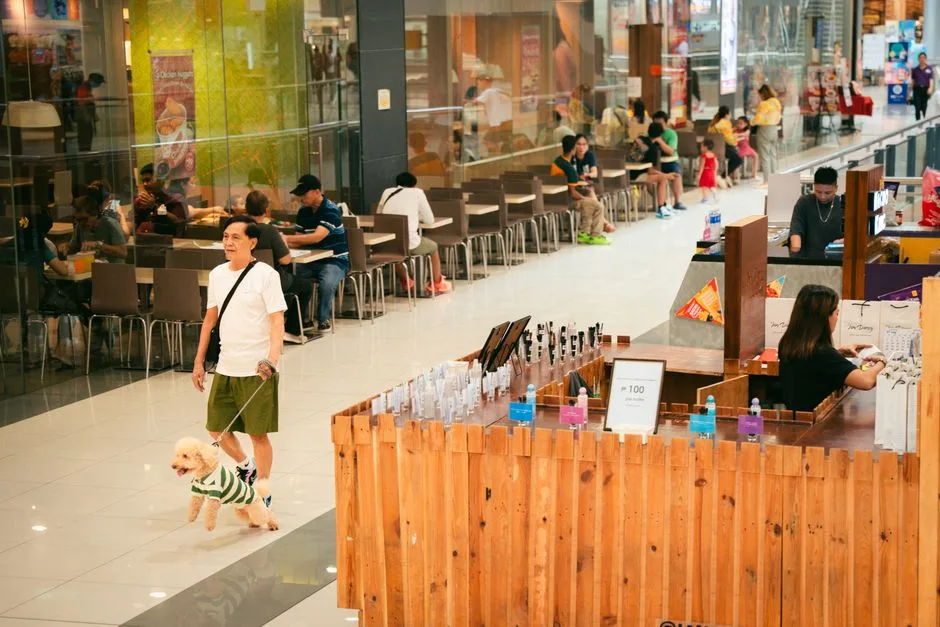 A lively indoor mall with people shopping and dining, featuring a man walking a dog.