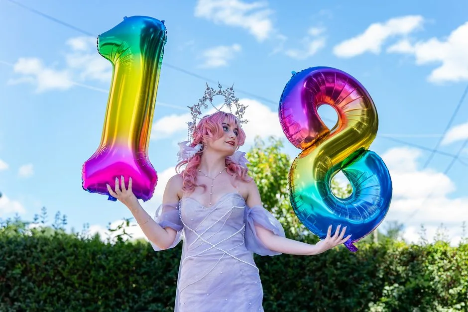 Young woman celebrating her 18th birthday with vibrant number balloons outdoors.