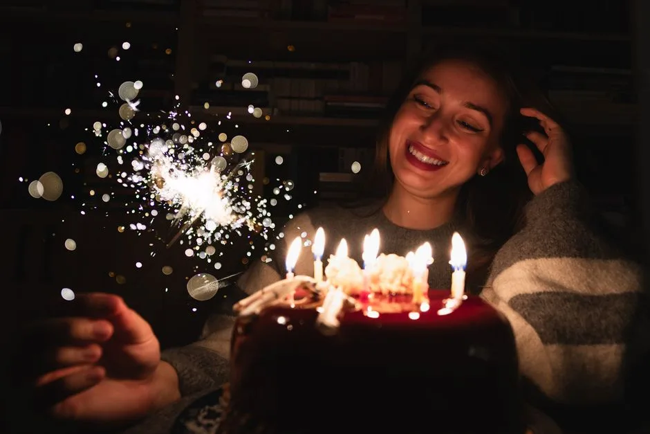 Smiling woman enjoying birthday cake with candles and sparkler indoors.