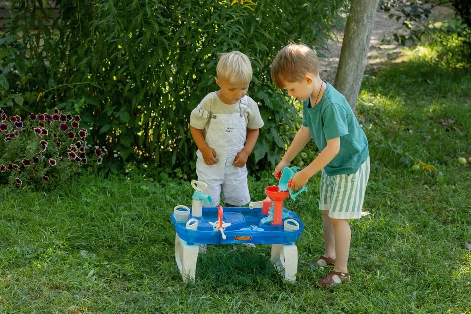 Two young boys engaged with a play table in a sunny garden setting, enjoying a fun summer day.
