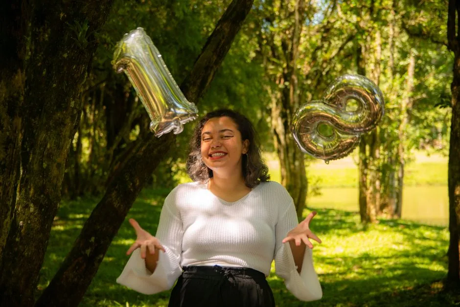 Smiling woman celebrating her 18th birthday outdoors with metallic balloons.